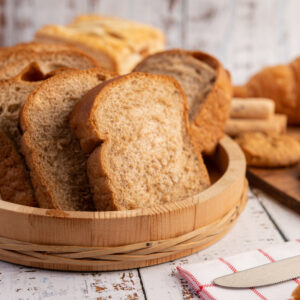 Bread slices placed in a wooden plate on a white wooden table. Selective focus.